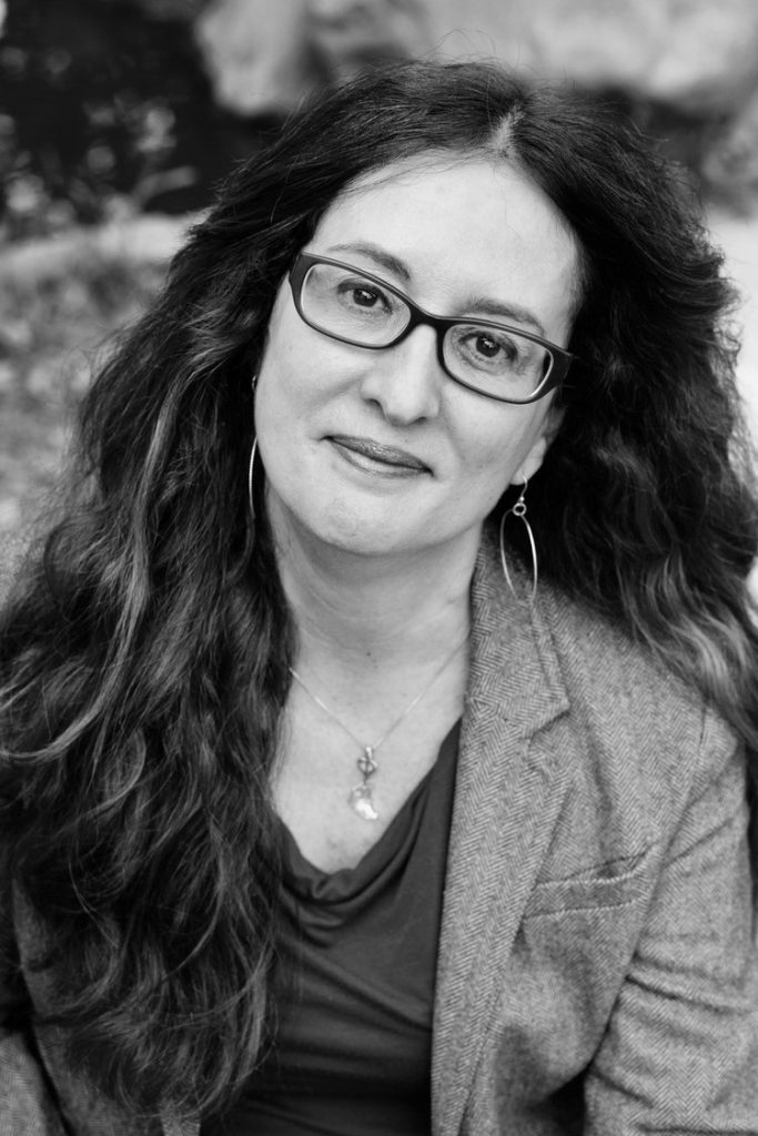Black-and-white portrait of a woman with long wavy hair, wearing glasses, hoop earrings, a necklace, a blazer, and a top, looking at the camera with a slight smile—capturing timeless style in Santa Barbara County.