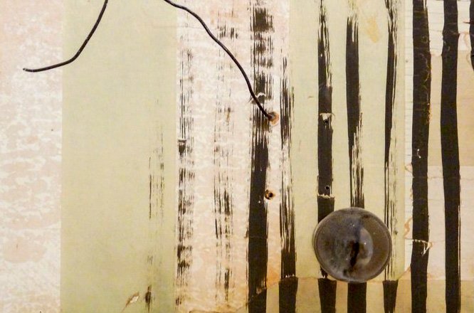 A close-up of a weathered, striped surface with vertical black lines on a faded light background, reminiscent of textures found in Santa Barbara County. A thin black wire and a round, translucent knob are attached to the surface.