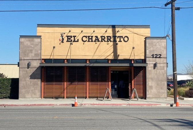 A tan and brown building with the sign El Charrito above the entrance. The number 122 is on the right side. Two orange traffic cones and two sandwich boards are on the sidewalk in front.